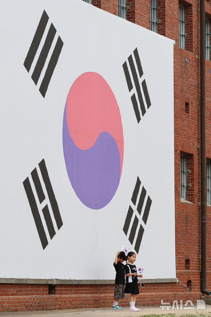 [서울=뉴시스] 권창회 기자 = 광복절을 하루 앞둔 14일 서울 서대문구 서대문형무소 역사관 대형 태극기 앞에서 아이들이 기념촬영을 하고 있다. 2026.08.14. kch0523@newsis.com