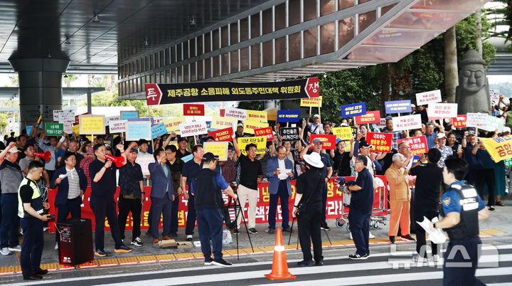[제주=뉴시스] 우장호 기자 = 공항 소음 피해 9개 읍·동 주민연대 관계자들이 14일 오후 제주국제공항 1층 도착장 3번 게이트 앞 도로 건너편에서 국토교통부와 공항공사를 상대로 공항소음지역 보상 현실화 요구 집회를 하고 있다. 2026.08.14. woo1223@newsis.com