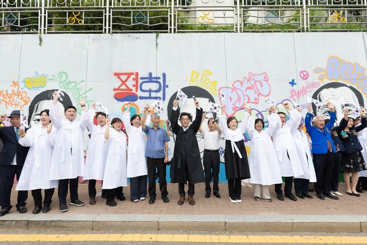 [수원=뉴시스] 15일 경기 수원시 매향여자정보고등학교에서 열린 광복 81주년 기념행사에서 참석자들이 '수원 독립운동의 길' 벽화 앞에서 태극기를 들고 만세 삼창을 하고 있다. (사진=수원시 제공) 2026.08.15. photo@newsis.com *재판매 및 DB 금지