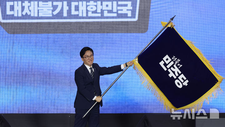 [대전=뉴시스] 정병혁 기자 = 김민석 신임 더불어민주당 당대표가 17일 대전 유성구 대전컨벤션센터 제2전시장에서 열린 더불어민주당 제3차 정기전국당원대회에서 당기를 흔들고 있다. (공동취재) 2026.08.17. photo@newsis.com