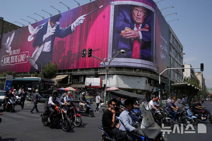 [테헤란=AP/뉴시스] 1일(현지시간) AP통신 등에 따르면 이란 남부 호르모즈간주 시리크 카운티의 쿠헤스타크에서 결혼식이 진행 중이던 주택이 미군 공격을 받았다. 사진은 지난달 31일(현지시간) 이란 테헤란 도심에서 오토바이 운전자들이 도널드 트럼프 미국 대통령의 모습과 함께 "속임수는 없다! 눈 깜빡하면 사라진다"는 문구가 그려진 대형 광고판 앞을 지나는 모습. 기사 본문과 사진은 직접 연관이 없음. 2026.09.02.
