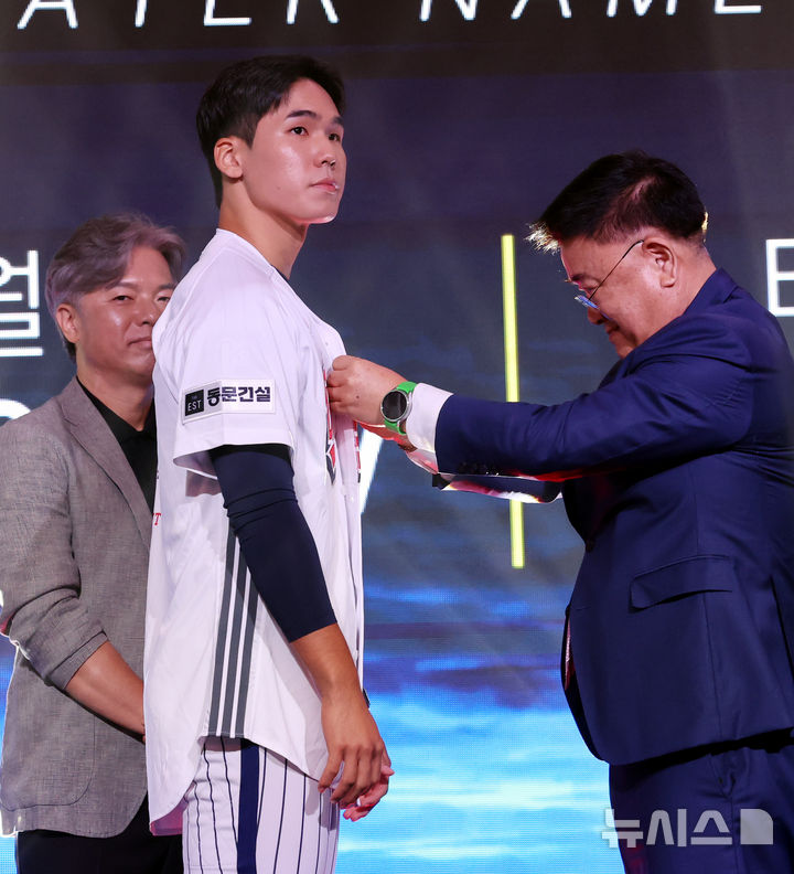 [서울=뉴시스] 박영태 기자 = 21일 오후 서울 송파구 롯데호텔 월드 크리스탈볼룸에서 열린 2027 KBO 신인 드래프트, 두산 김태룡 단장이 전체 2순위로 서울고 김지우를 지명한 후 유니폼을 입혀주고 있다. 2026.09.21. since1999@newsis.com