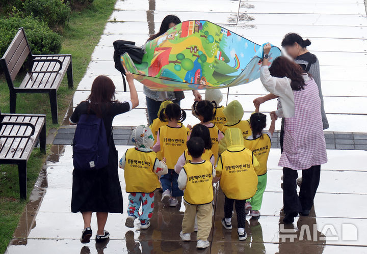  [부산=뉴시스] 하경민 기자 = 갑자기 비가 내린 지난달 29일 부산 동구 북항 친수공원에서 어린이집 교사들이 돗자리를 펼쳐서 대형 우산을 만들어 원생들과 이동하고 있다. 2026.09.29. yulnetphoto@newsis.com