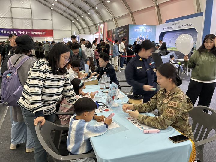 [계룡=뉴시스]곽상훈 기자=3일 계룡대 활주로에서 열린 군문화축제에서 어린이 관람객이 공군의 폭발물처리 부대 여성 군인으로부터 공군캐릭터 그리기 도움을 받고 있다. 2026.10.03 photo@newsis.com *재판매 및 DB 금지