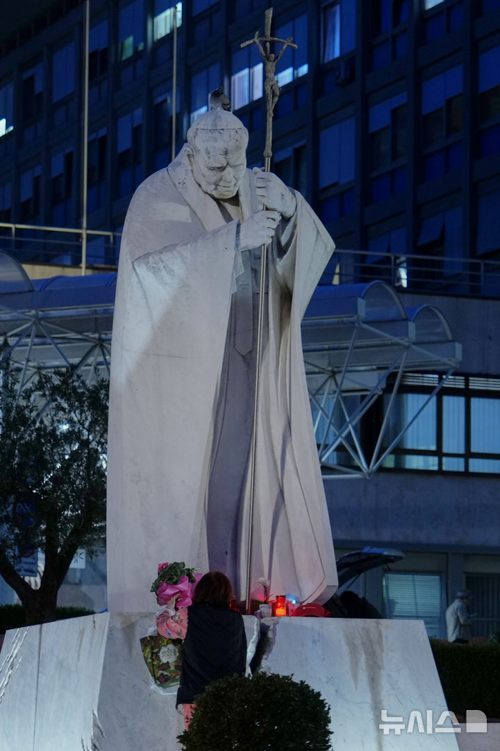 [로마=AP/뉴시스] 12일(현지 시간) 교황 레오 14세가 입원할 이탈리아 로마의 아고스티노 제멜리 종합병원에서 한 여성이 요한 바오로 2세 전 교황 동상 아래 레오 14세 교황의 쾌유를 기원하는 꽃과 촛불을 놓고 있다. 레오 14세 교황은 이곳에서 폐 결절 수술을 받을 예정이다. 2026.10.12.