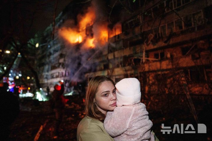 [AP/뉴시스] 13일 우크라 키이우에 러시아 미사일이 날아와 화재가 나고 어머니가 아기를 안고 대피하고 있다