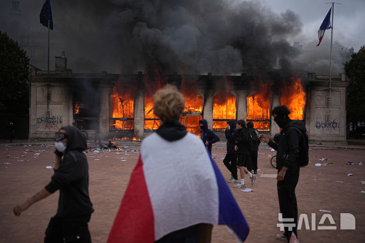 A protester wraps a French flag around them in front of the burning tourism office during a demonstration against rising living costs and in solidarity with students’ grievances in Lyon, France, Saturday, Oct. 17, 2026.(AP Photo/Laurent Cipriani)