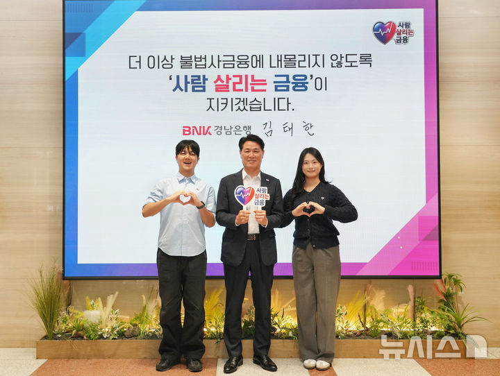 [창원=뉴시스]BNK경남은행 김태한(가운데) 은행장이 창원 본점에서 남녀 직원과 함께 '사람 살리는 금융 릴레이 캠페인' 참여 퍼포먼스를 하고 있다.(사진=BNK경남은행 제공) 2026.10.19. photo@newsis.com